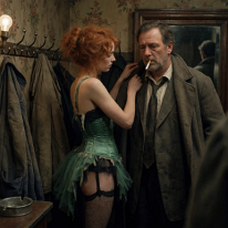 A Fleeting Moment of Tender Service In a dim cloakroom, a young woman in a faded corset and laddered stockings helps a car salesman into his overcoat. Her focused, patient expression and his...